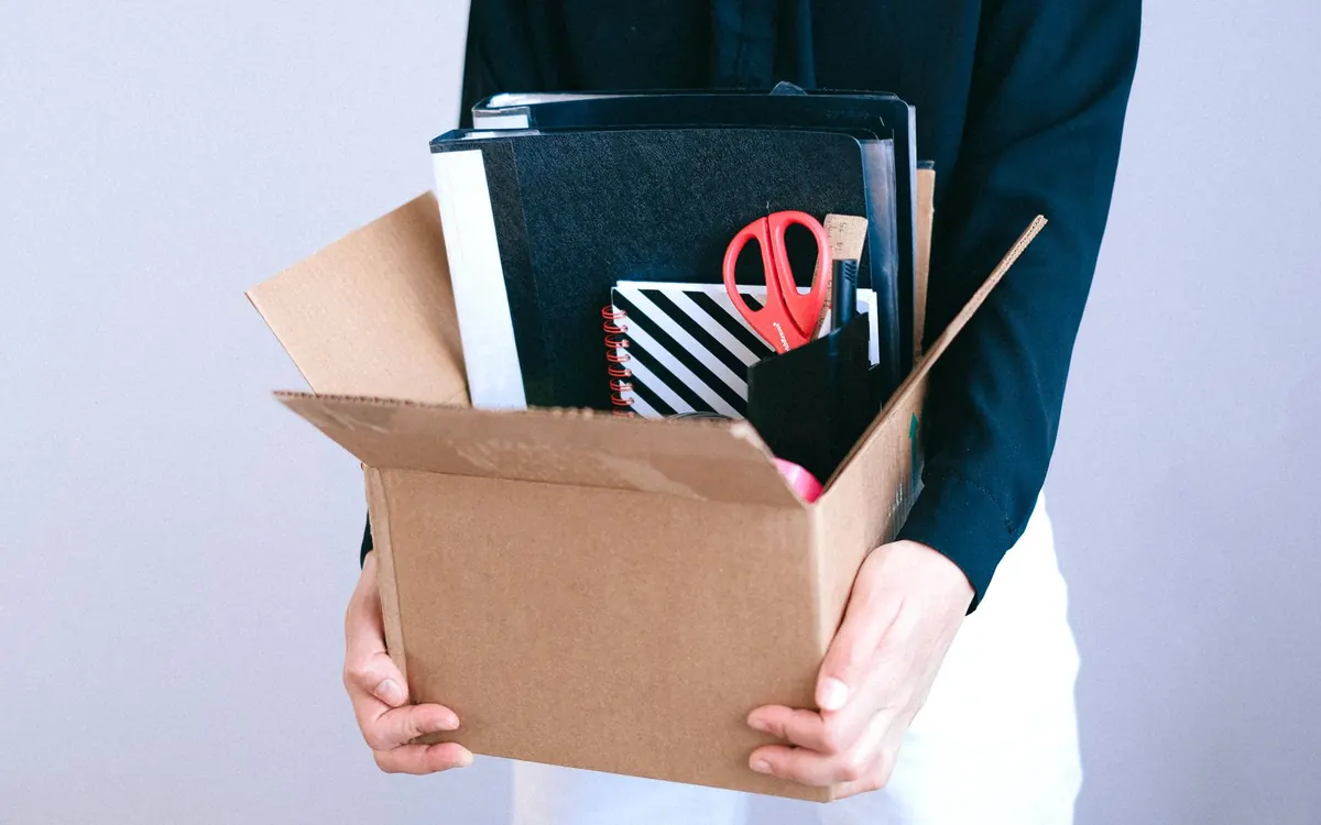 Eine Person trägt einen Karton mit Büroordnern und Schreibwaren