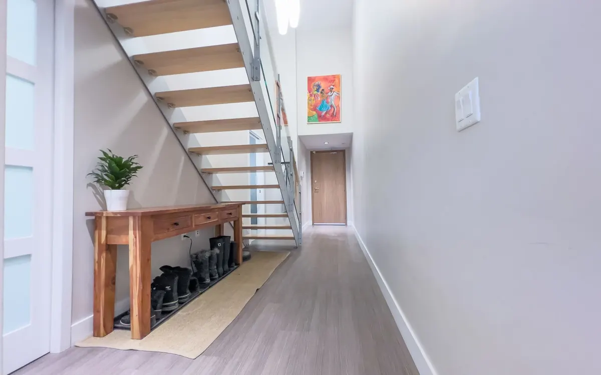 Ein heller Wohnungsflur verläuft unter einer offenen Treppe