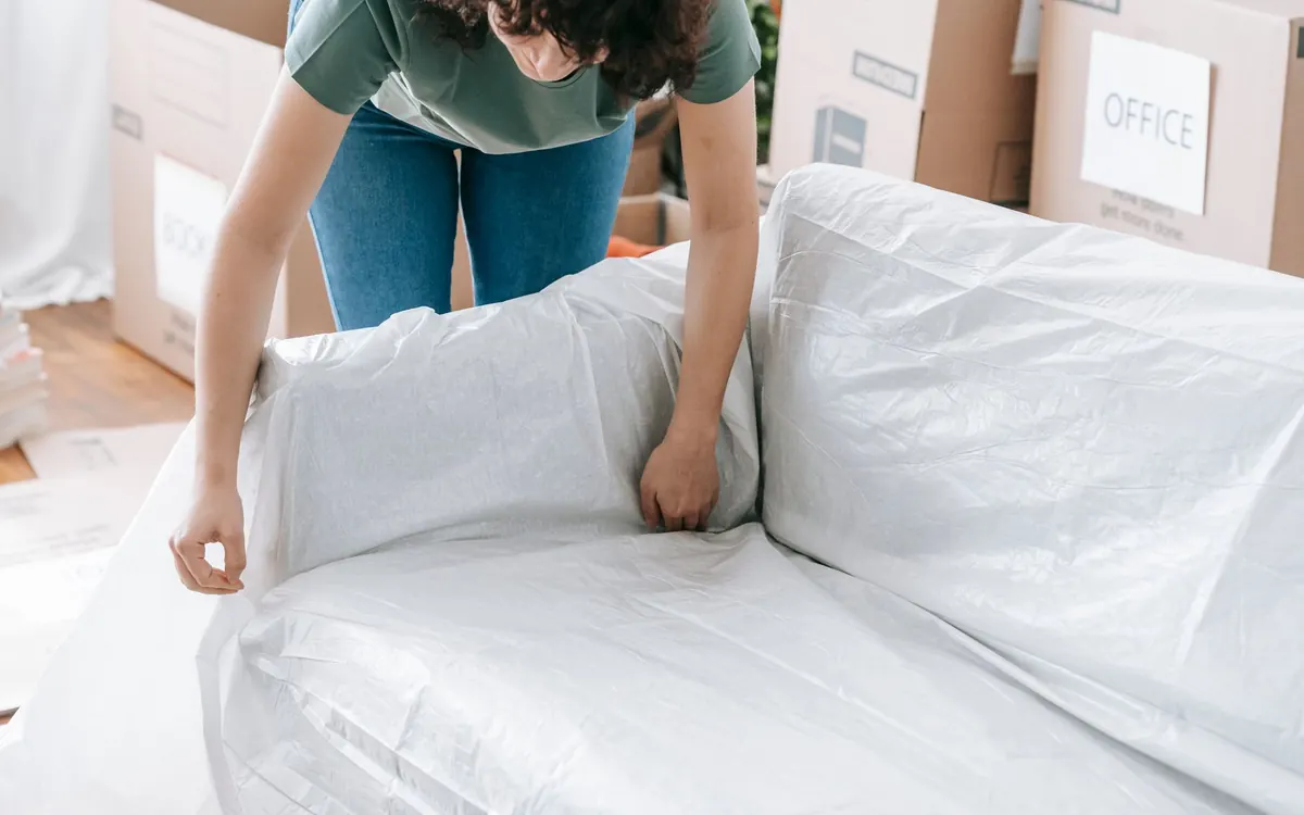 Eine Person schützt ein Sofa mit einer weißen Transporthülle