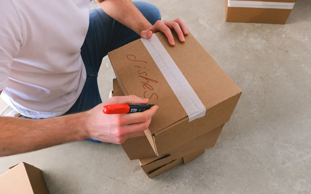 Ein gepackter Karton wird mit Inhalt und Zielraum beschriftet