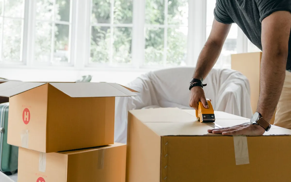 Hände verschließen einen gepackten Karton mit Klebeband