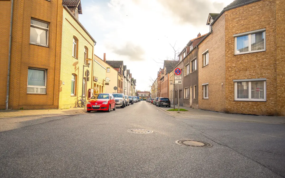 Eine Wohnstraße führt an Häuserzeilen und geparkten Autos vorbei
