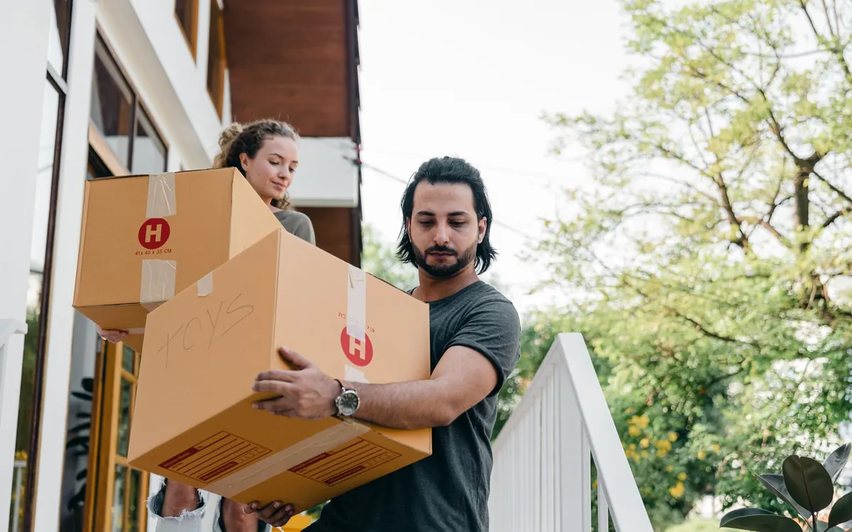 Zwei Personen tragen Umzugskartons über einen Gehweg