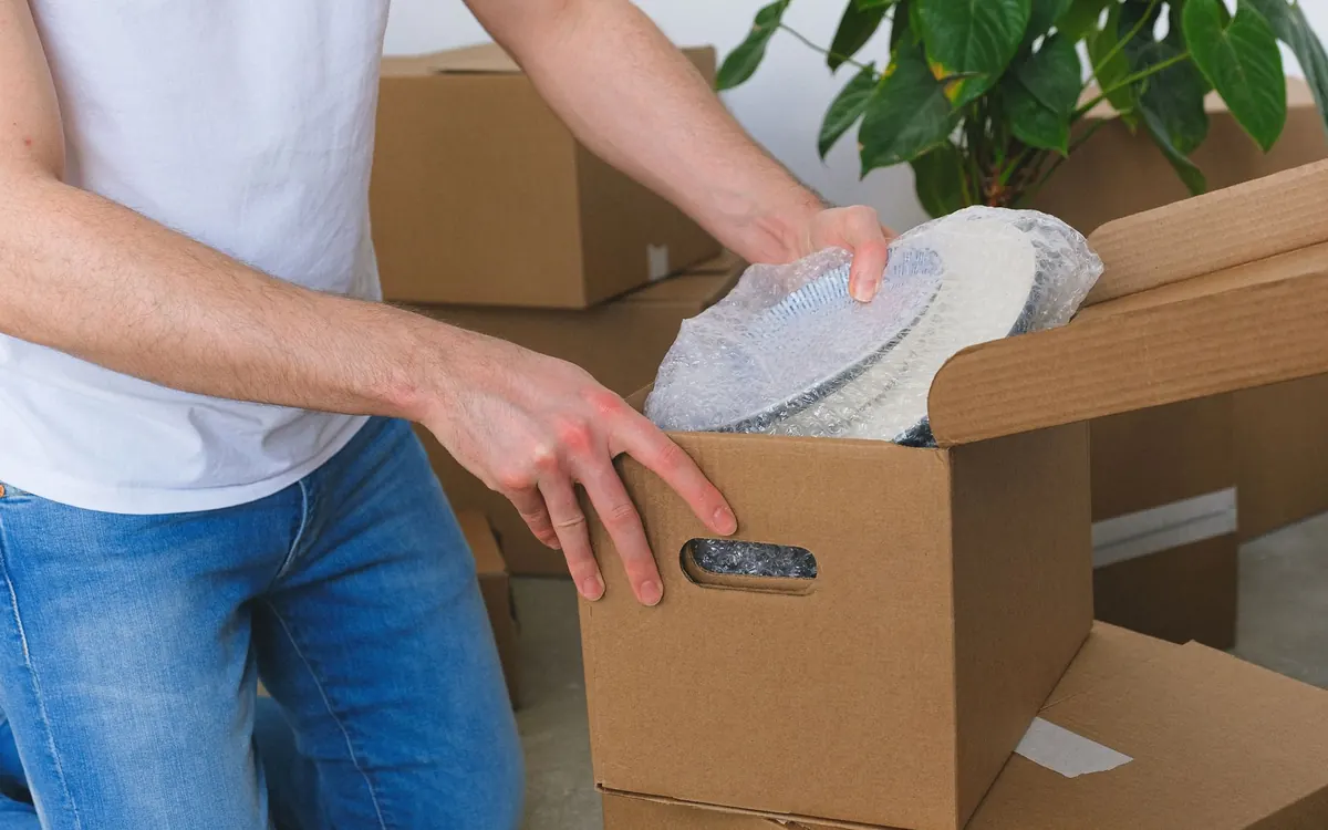 Hände verpacken einen empfindlichen Gegenstand in einem Karton