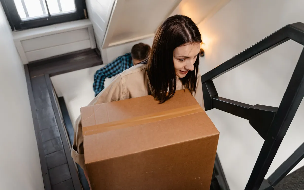 Zwei Personen tragen einen großen Karton gemeinsam eine Treppe hinauf